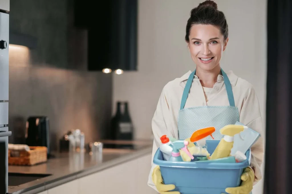 Friendly professional cleaner at a client's home with cleaning supplie